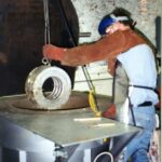 A prepared babbitt bearing shell being lowered into a molten tinning bath furnace